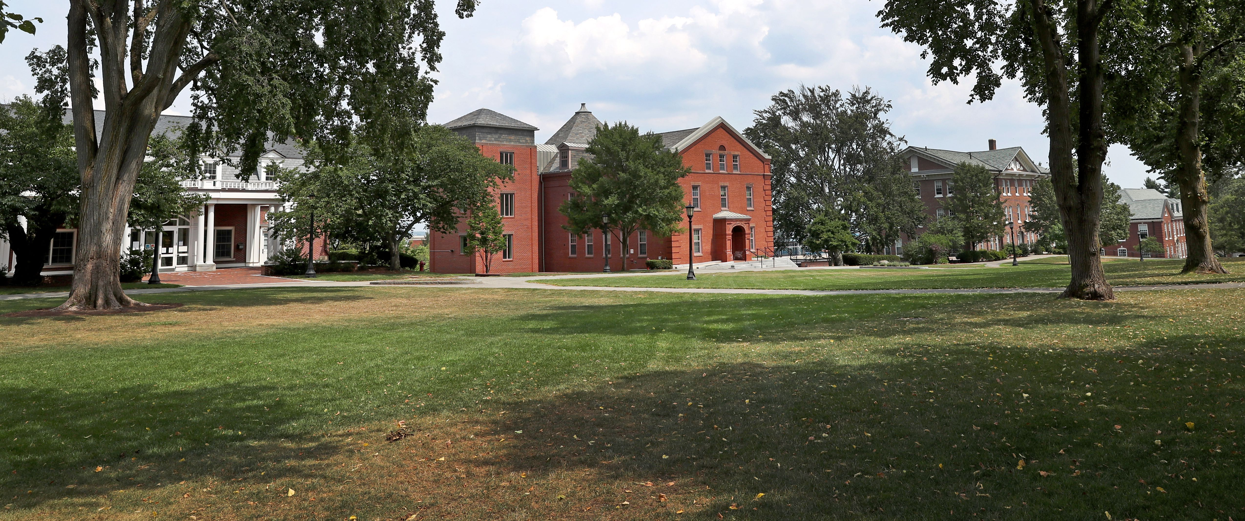 A college campus with a green yard in the foreground and red brick buildings in the distance